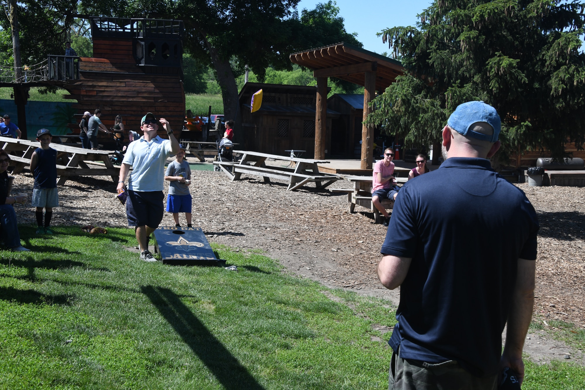 Master Sgt. Bryan Johnson, 1st Weather Group, pitches a bag against Chief Master Sgt. Kevin Paul, 557th Weather Wing command chief, during a game of Cornhole at the 2021 557th Weather Wing Picnic at the Bellevue Berry Farm on June 4, 2021 in Bellevue, Nebraska.