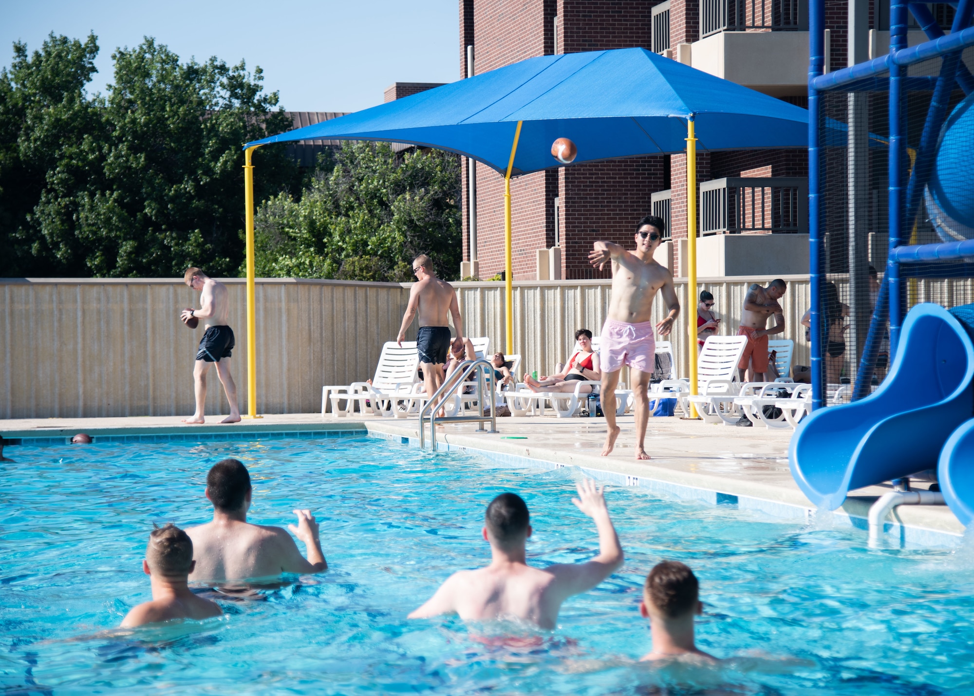 Members of Goodfellow Air Force Base throw a football at the Mcgarr Pool during the 17th Force Support Squadron Block Party, on Goodfellow AFB, Texas, June 11. During the event, members were able to enjoy free bowling, the Mcgarr Pool, inflatable water slides, food trucks and various outdoor games. (U.S. Air Force photo by Staff Sgt. Tyrell Hall)