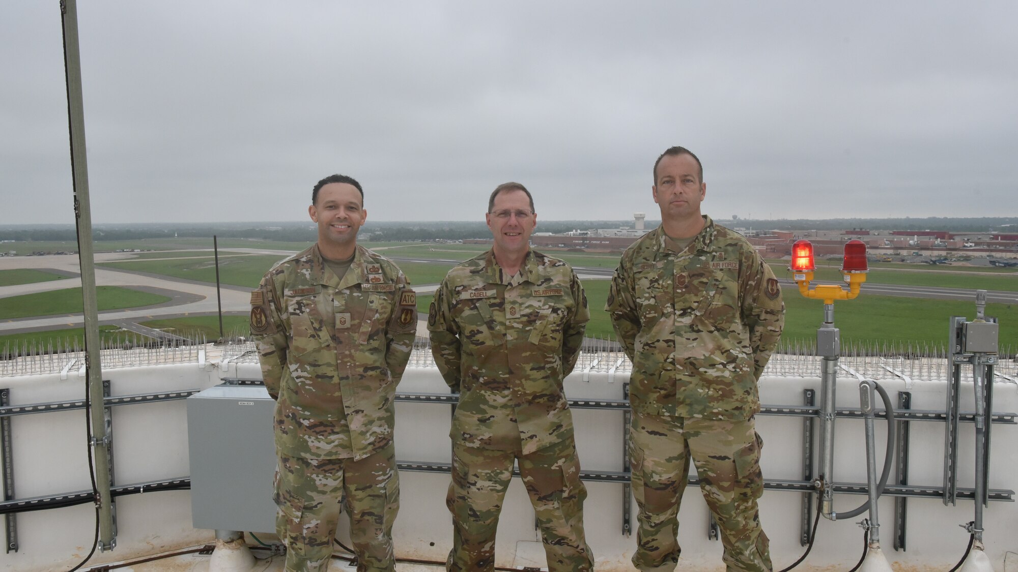 Three Airmen standing on top of air traffic control tower.