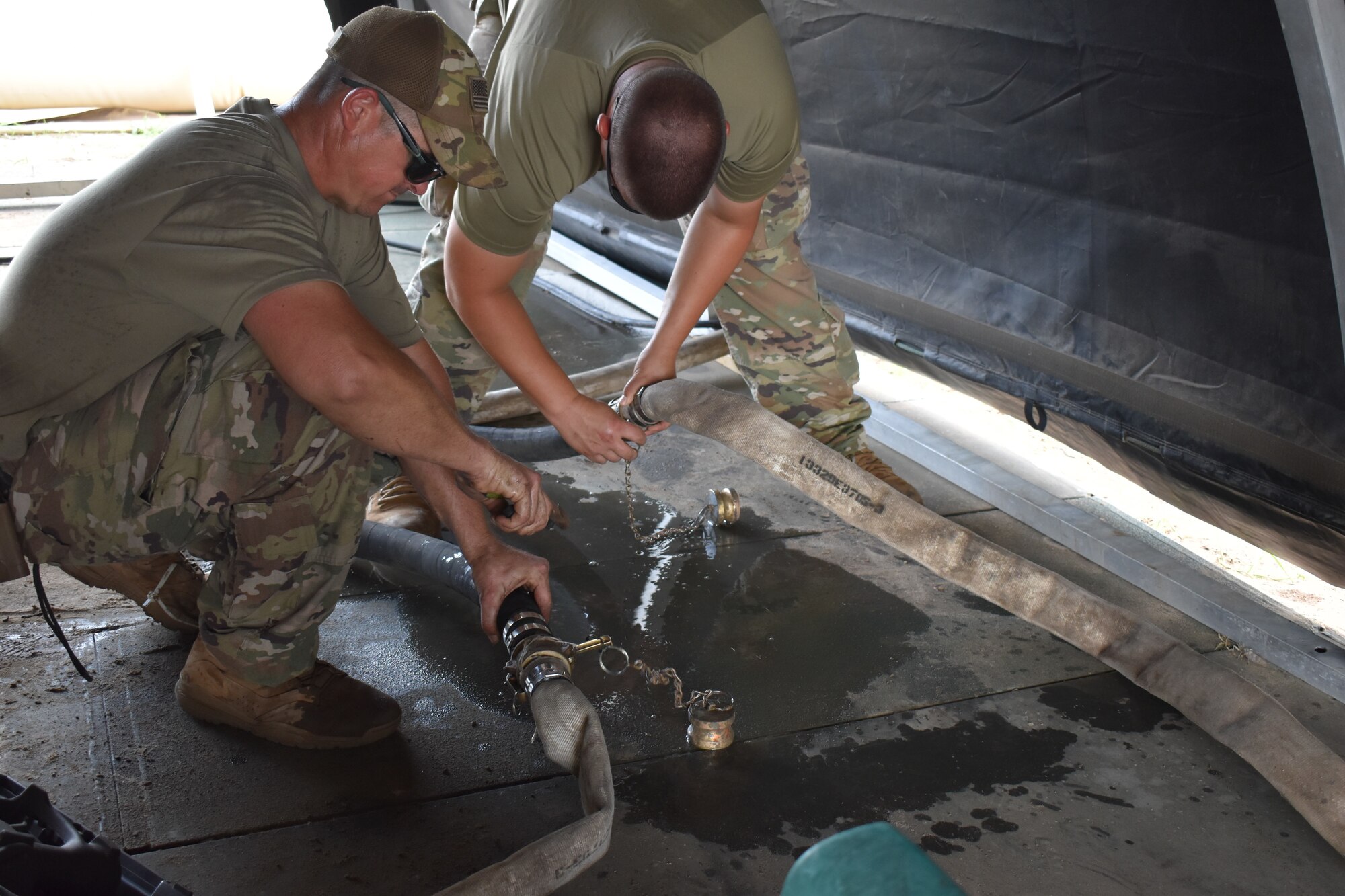 Tech. Sgts. Jerl Dunn and Brendan Muchow, water and fuels system maintenance craftsmen for the 776th Expeditionary Air Base Squadron connect a hose at Camp Simba at Manda Bay, May 19, 2021. The technicians installed several reverse osmosis water purification units (ROWPU) which are used to purify and sanitize water for drinking and personal hygiene use at Camp Simba.