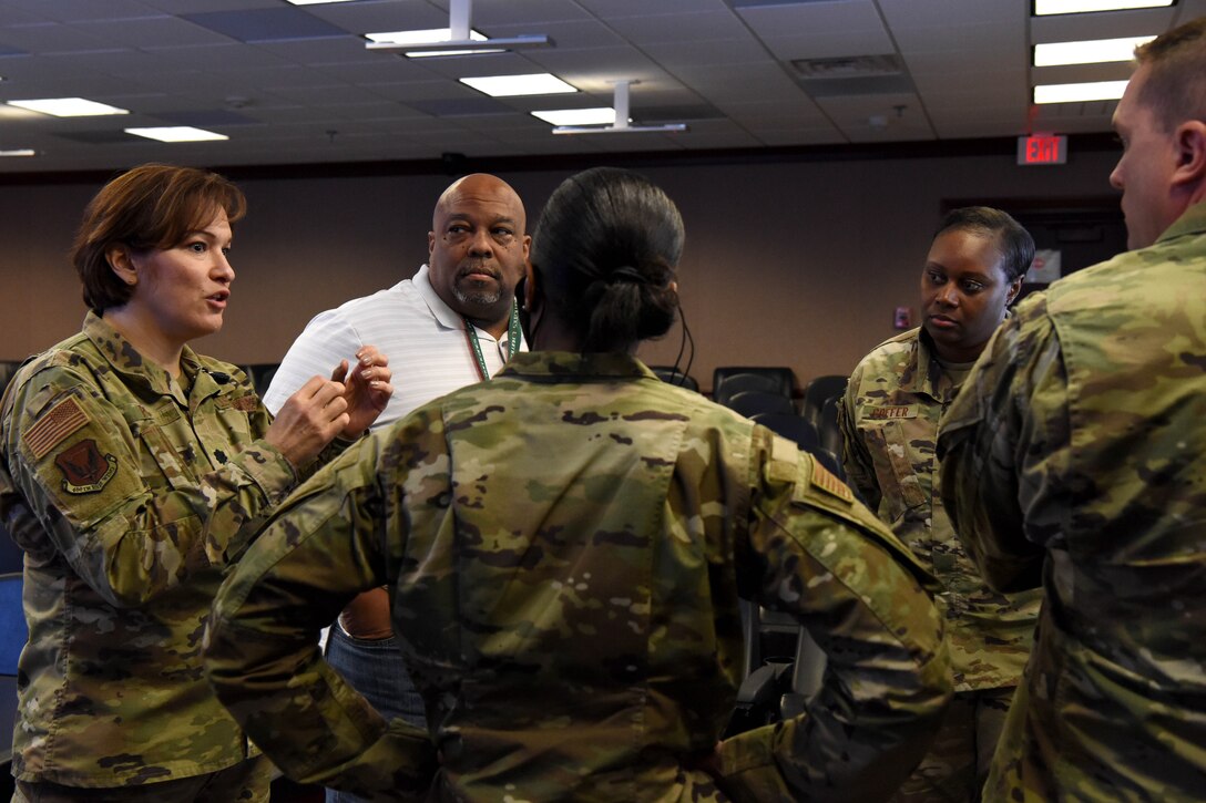 Five Airmen stand in a circle listening while one Airman speaks.