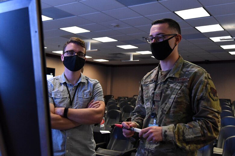 Two men stand in front of a screen.