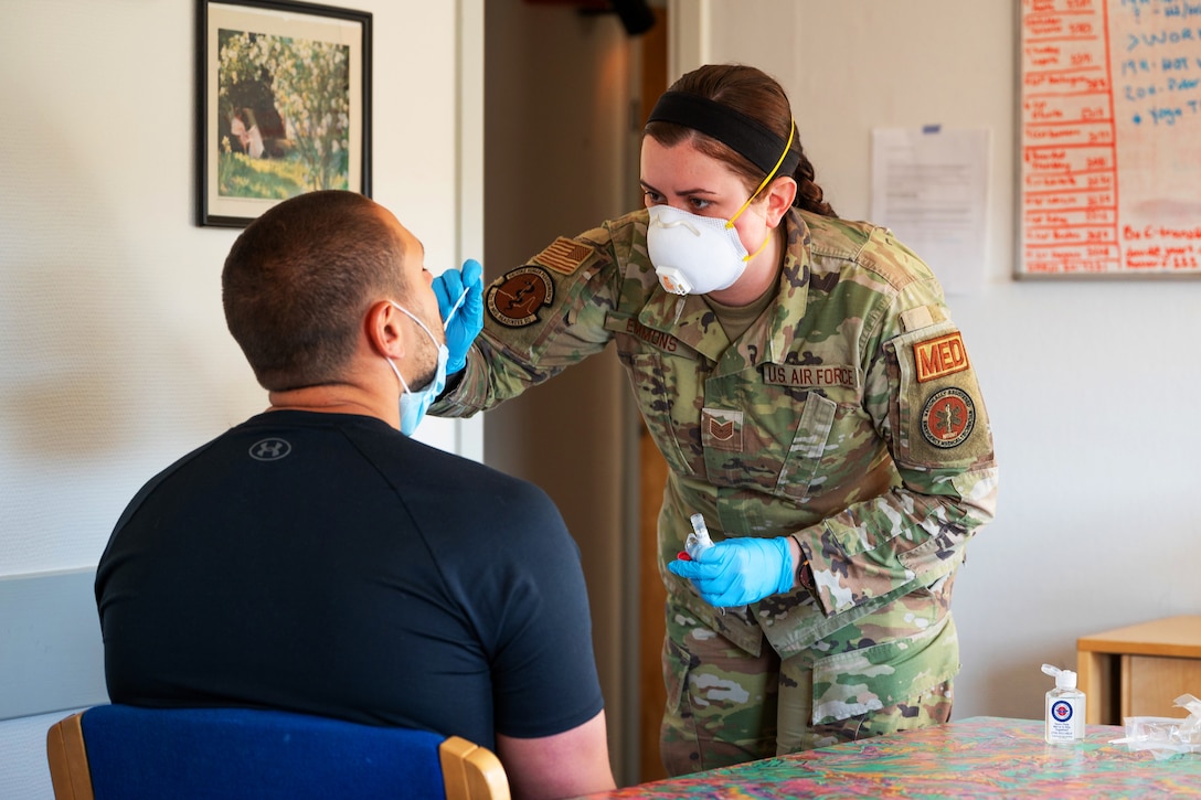An airman wearing a face mask and gloves holds a nasal swab while administering a COVID-19 test.