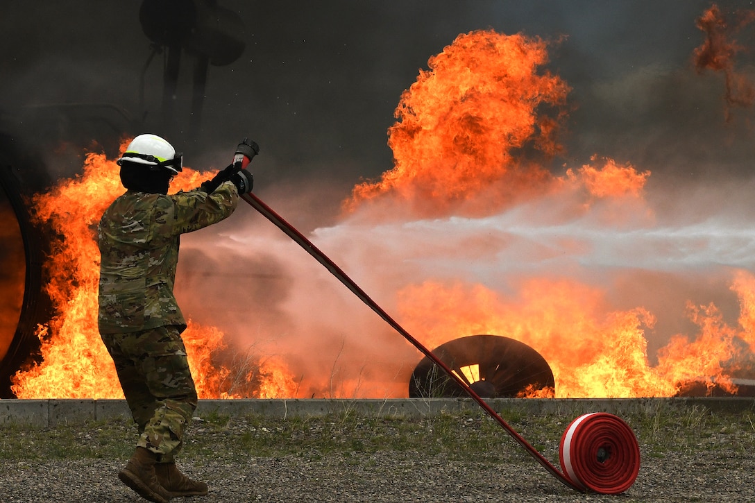 An airman prepares to use a water hose to put out a fire.