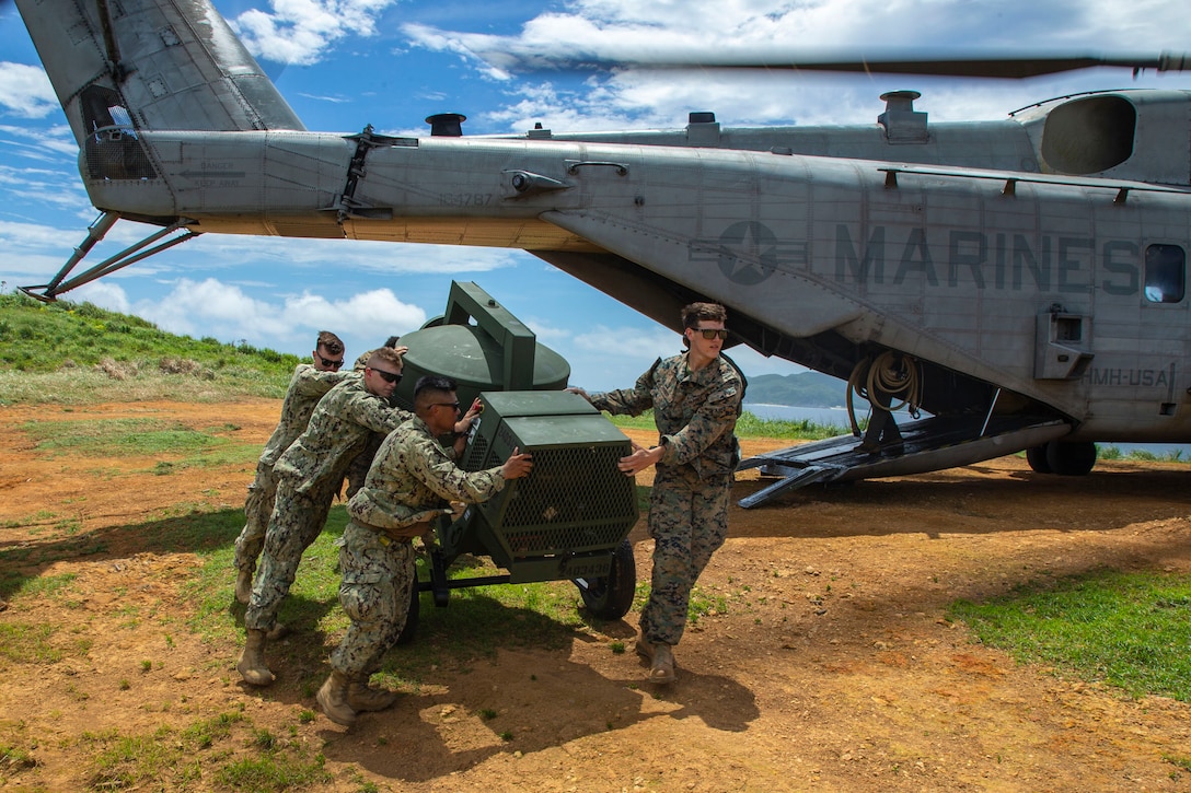 Marines and sailors offload equipment from a helicopter.