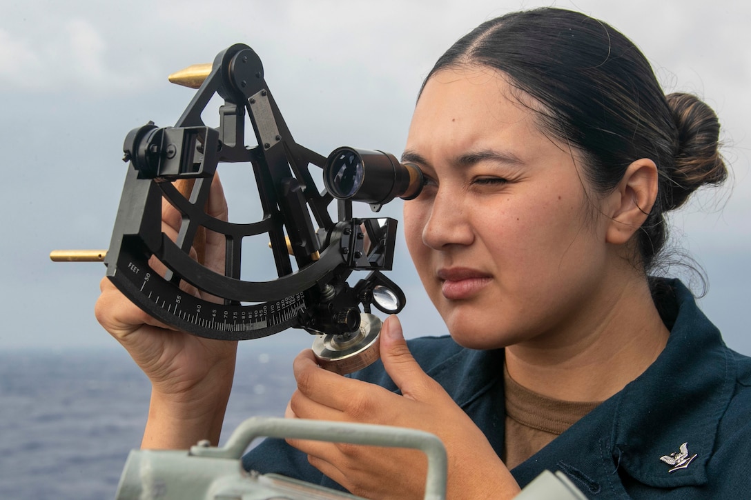 A sailor looks through a sextant.