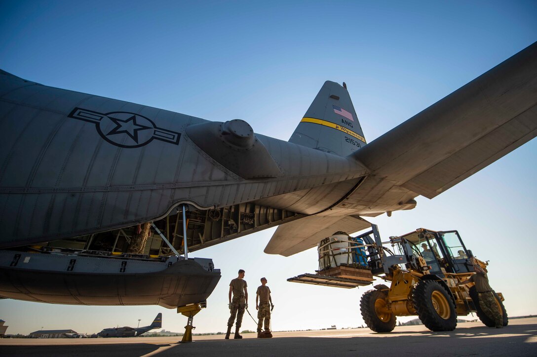 A guardsman uses a forklift to load equipment onto an aircraft as two others stand and watch.