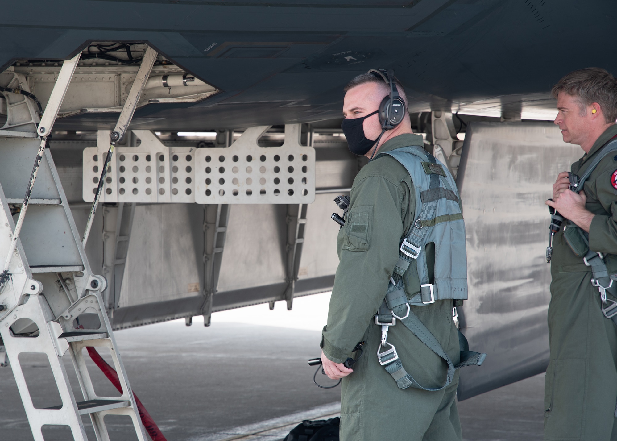 A U.S. Air Force Airman wearing a green flight suit approaches the crew ladder of a B-2 Spirit stealth bomber before a flight.