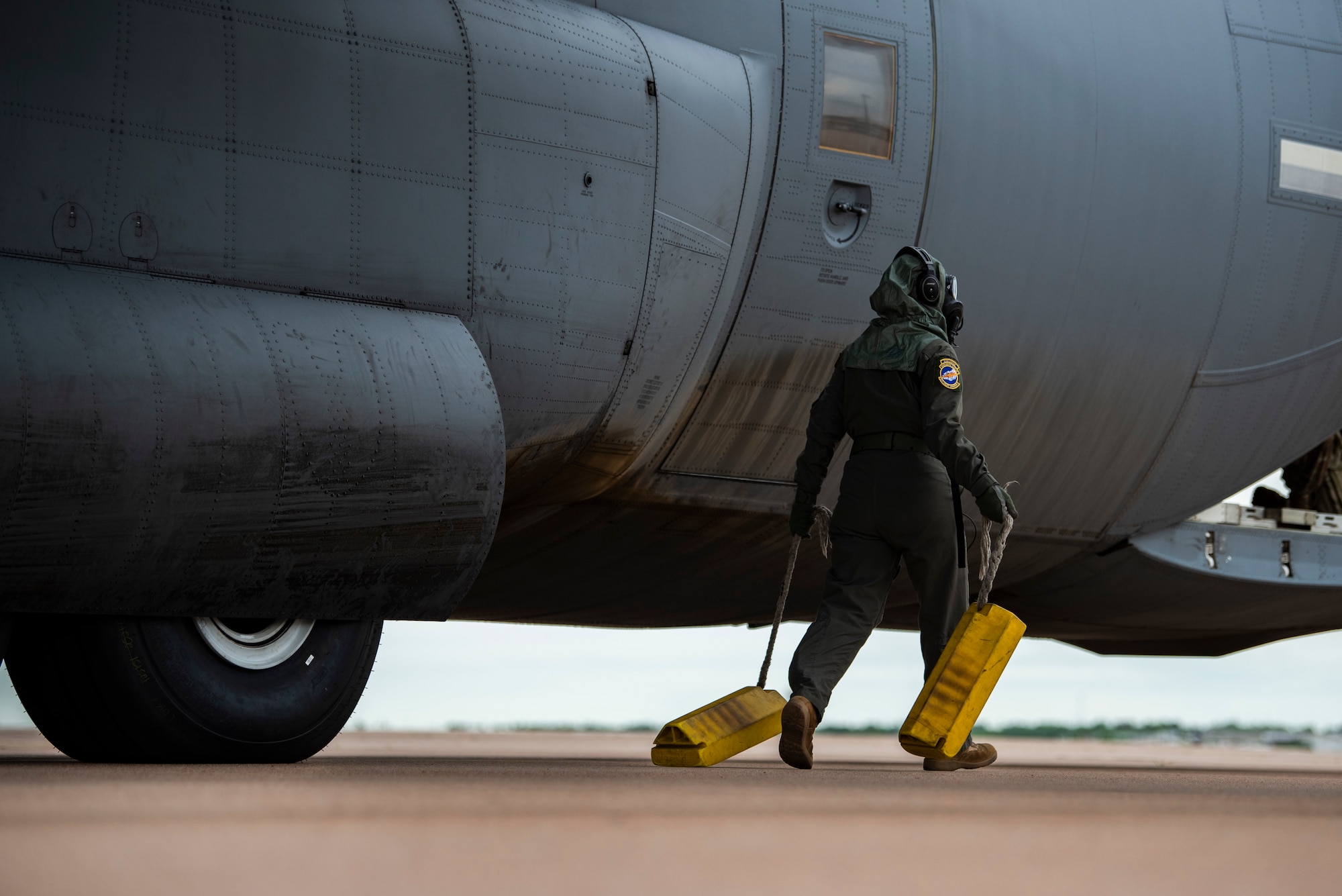Staff Sgt. Tristan Geray, 40th Airlift Squadron loadmaster, drags tire chocks next to a C-130J Super Hercules at Dyess Air Force Base, Texas, June 3, 2021. C-130J aircrew conducted field testing of the new Two-Piece Undergarment universal integrative ensemble chemical protective suit to assess the equipment's functionality. (U.S. Air Force photo by Airman 1st Class Colin Hollowell)