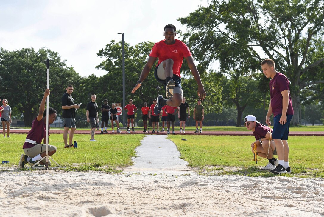 An airman jumps through the air during a long jump event while others look on.