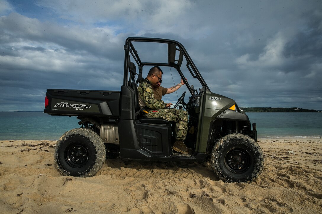 Two service members sit in a vehicle on the beach.