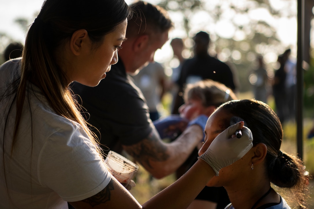 An airman uses a tool to create a fake wound on another airman's head.