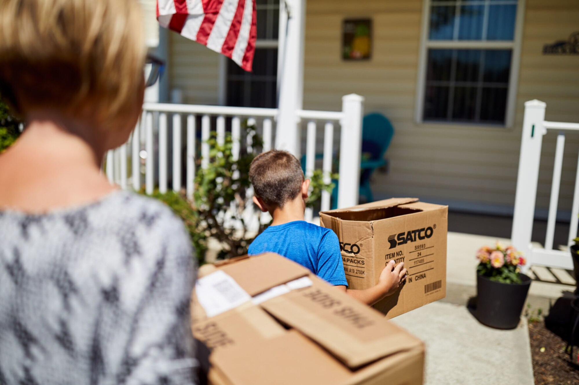 Woman and child carry moving boxes while walking into a house.