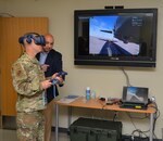 Lt. Gen. Timothy Haugh wears a headset while holding a remote control in his hands during a virtual reality demonstration.