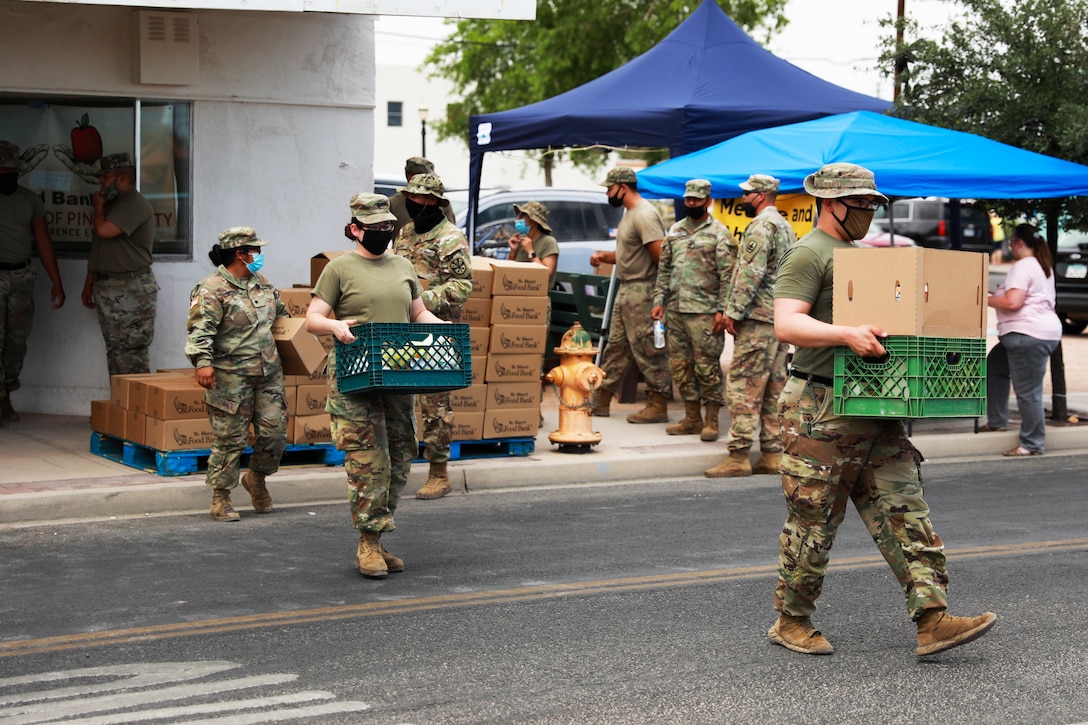 Guardsmen wearing face masks carry boxes and crates across a street.
