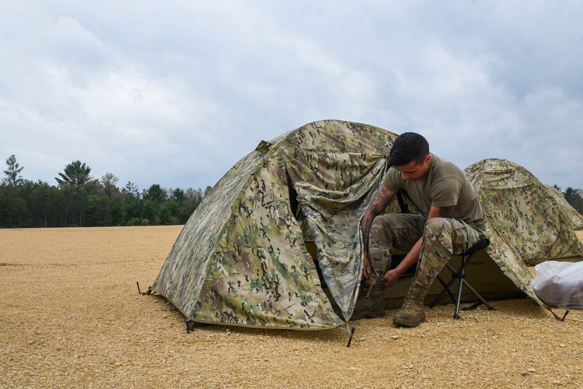 A photo of an airmen tying his boot outside of a tent