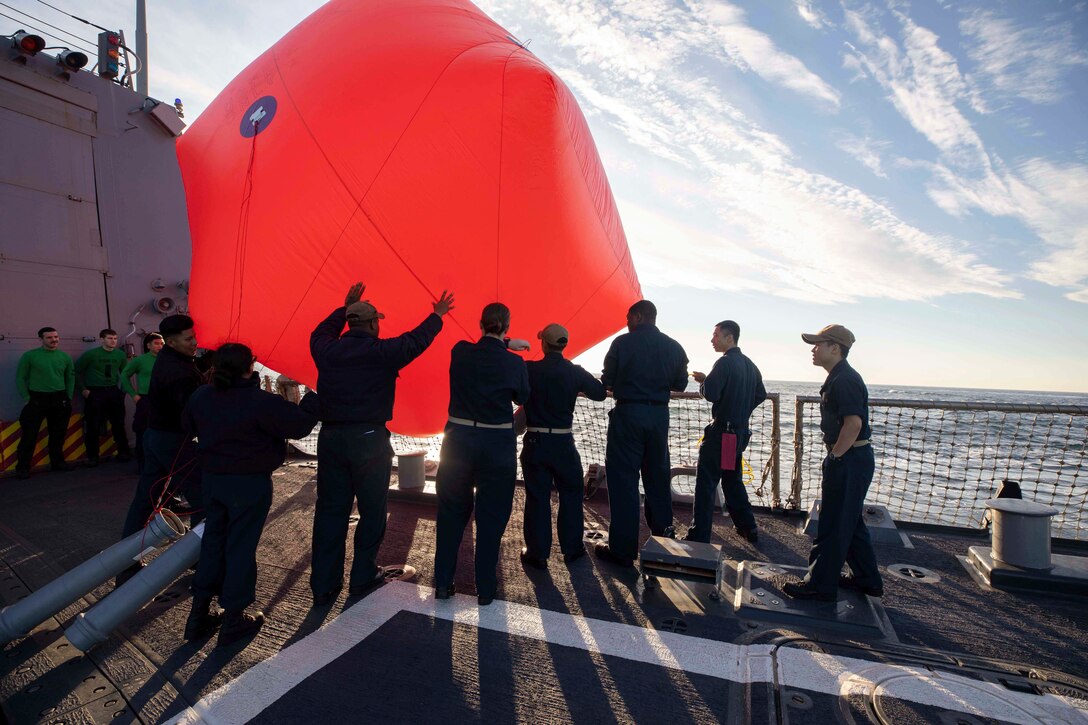 Sailors throw a red inflatable target into a body of water from a ship.