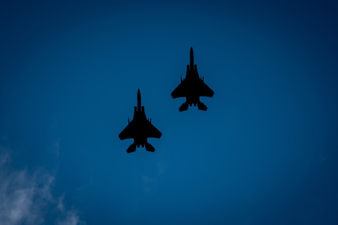 Two aircraft are seen in silhouette against a blue sky.