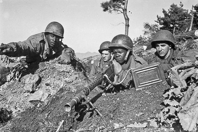 One soldier points from behind an embankment as others look to see what he's indicating.