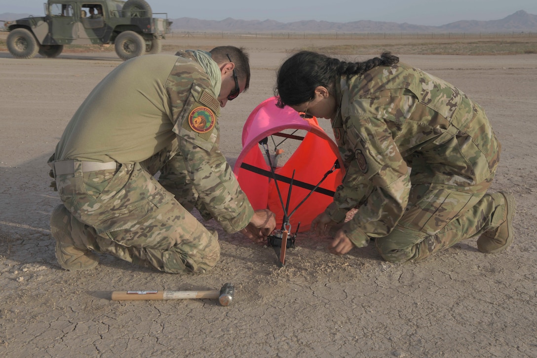 Two airmen secure a runway light on a dirt road.