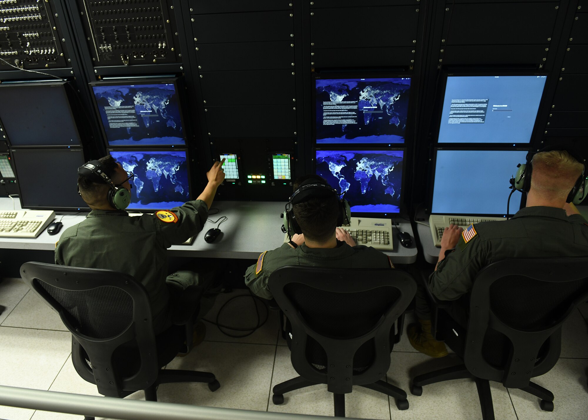 Three Airmen in uniform sit in front of computer screens for a new flight simulator.