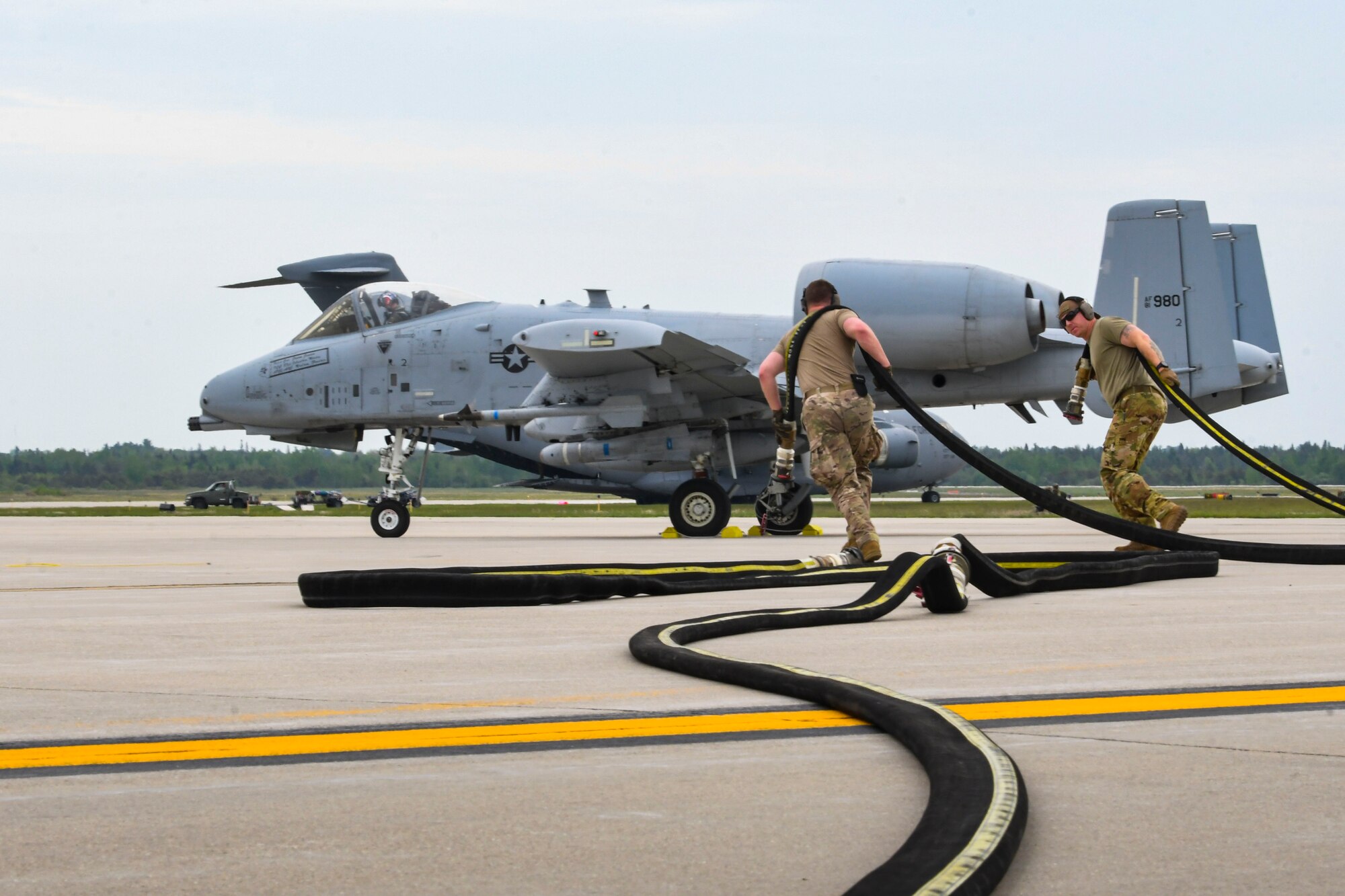 A photo of two airmen pulling a fueling hose to an aircraft