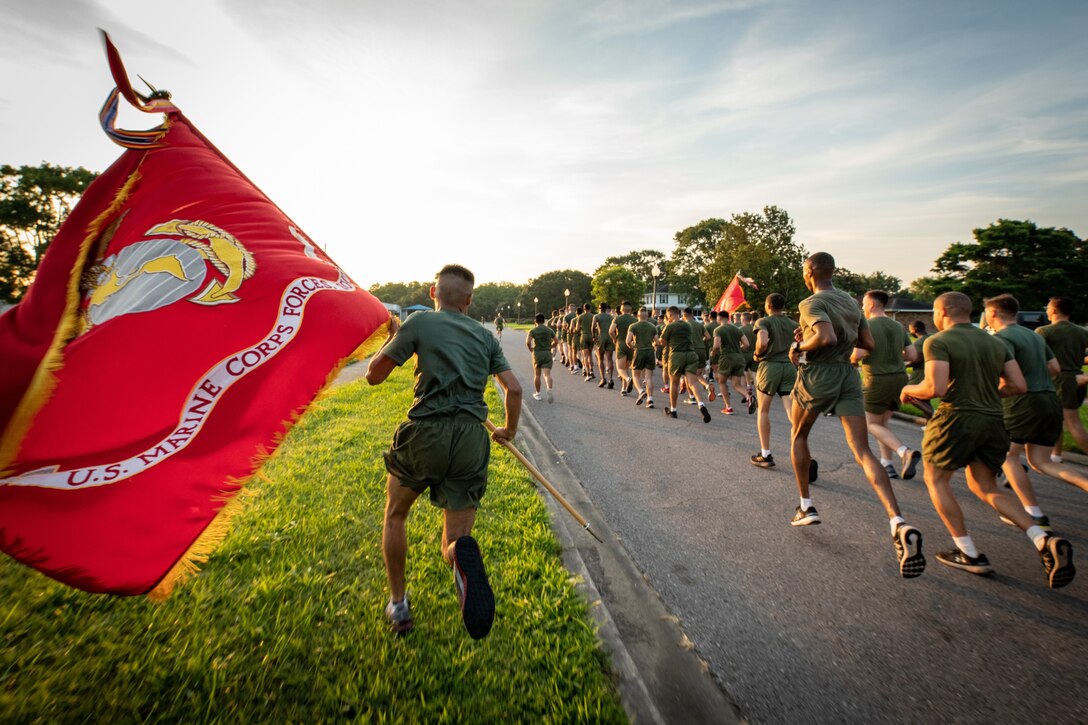 A Marine carries a large flag alongside a large group of runners.