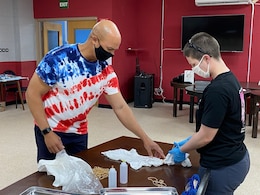 Maj. Anthony Sims-Hall, 1st Theater Sustainment Command, theater mortuary affairs officer, instructs a Soldier on tie-dying techniques at an event held at the MWR building on Camp Arifjan, Kuwait.  Maj. Sims-Hall takes personal passion and hobbies and turns them into resiliency opportunities for Soldiers while deployed.