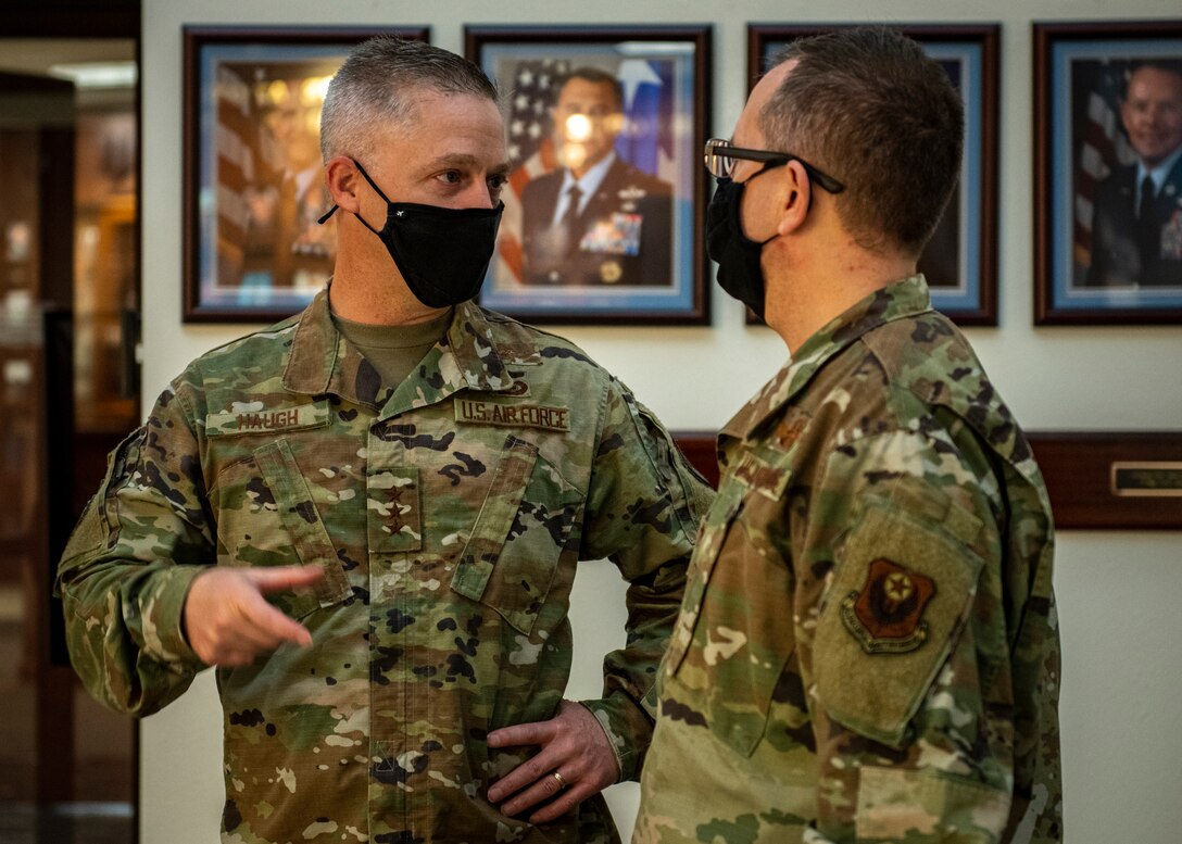 Two Airmen speak while standing in a hallway in front of Air Force portraits.