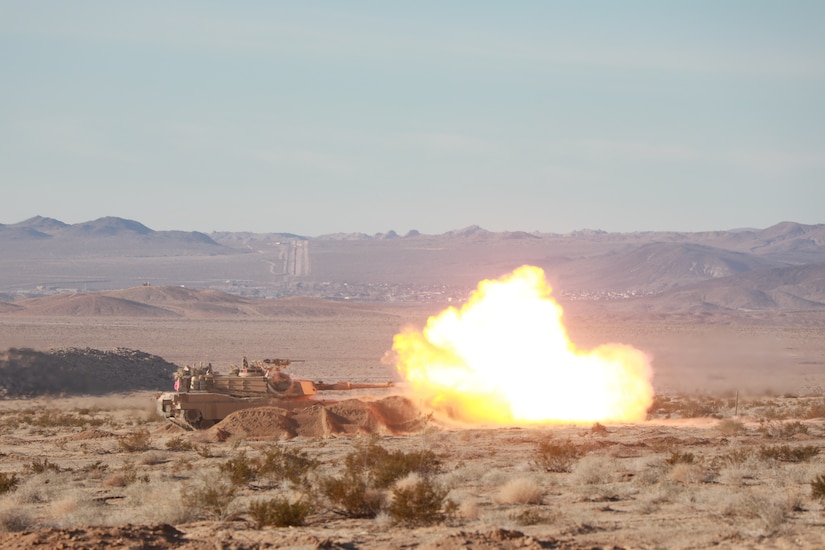 A ball of fire erupts from a tank as it fires on a desert landscape.