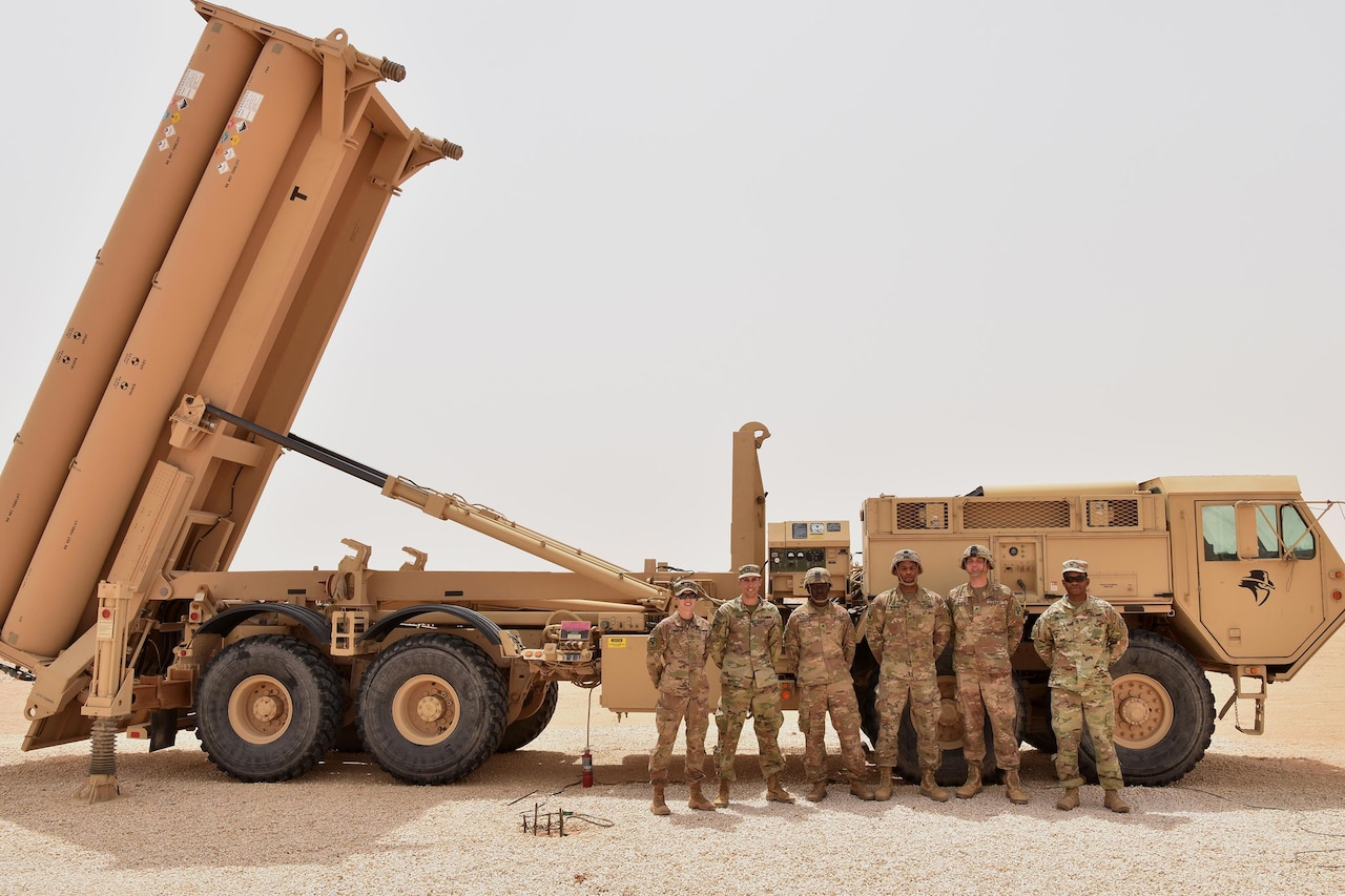 Soldiers stand beside a missile launcher.