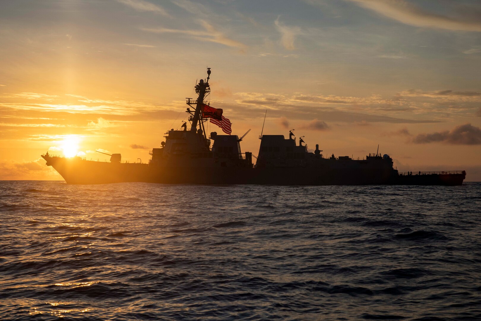 A ship sails with the sunset as backdrop.