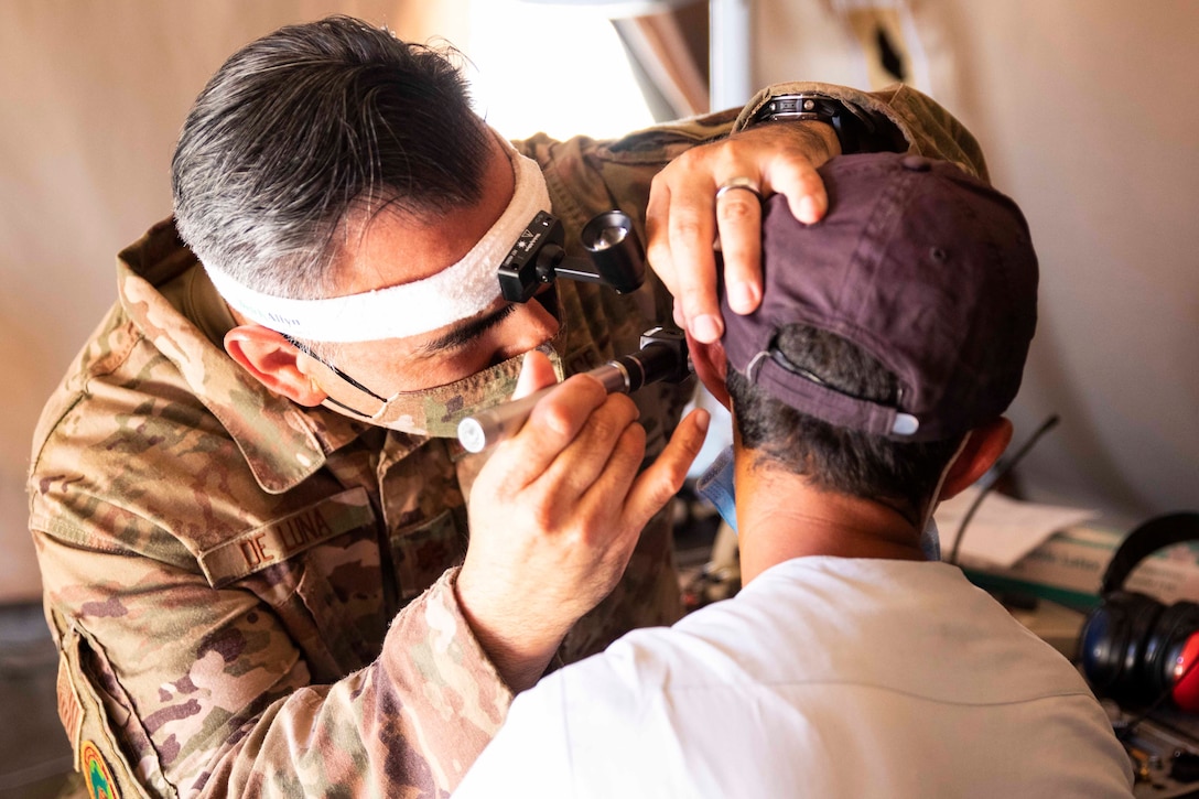 An airman uses a tool to look into a person’s ear.
