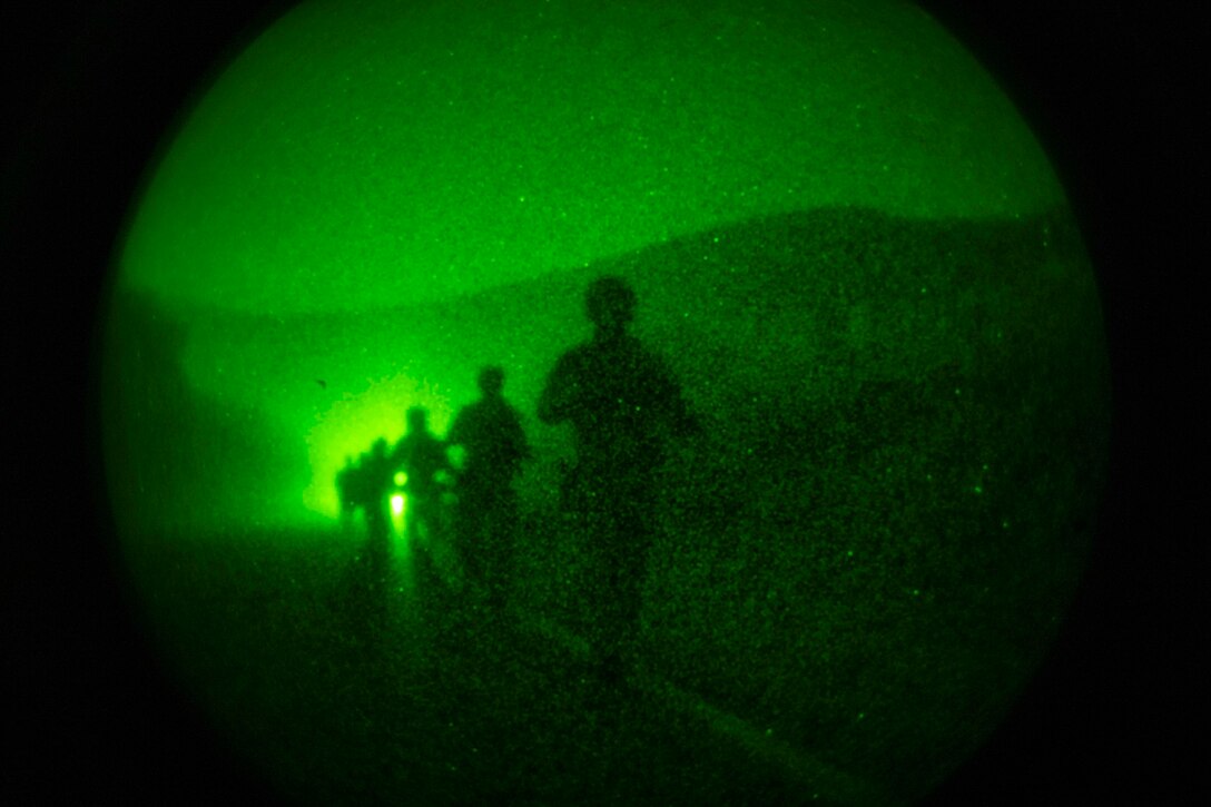 Navy SEALs shown in silhouette walk in a line holding weapons.