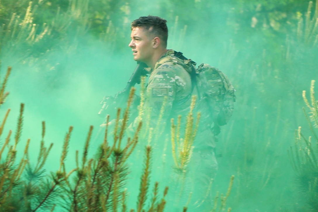An airman moves through a wooded area surrounded by green smoke.