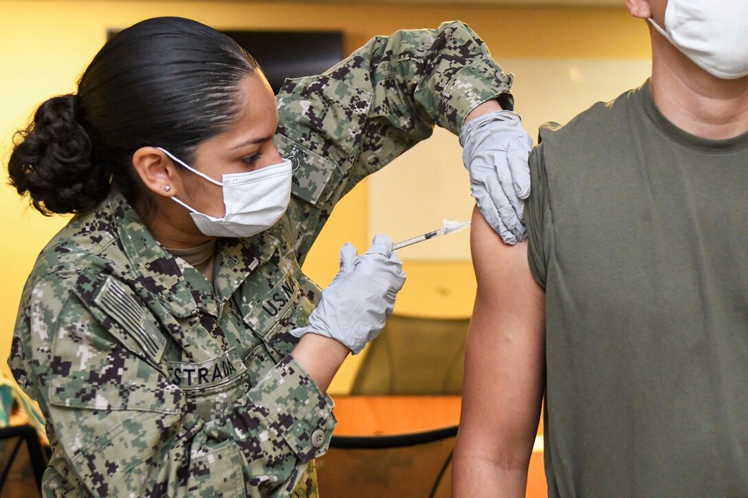 A sailor wearing a face mask and gloves gives a COVID-19 vaccine to a Marine.