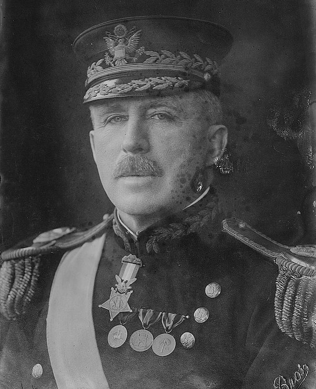 A man in military dress with many decorations looks at the camera.