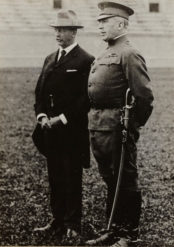 A military officer stands with a man in a business suit.