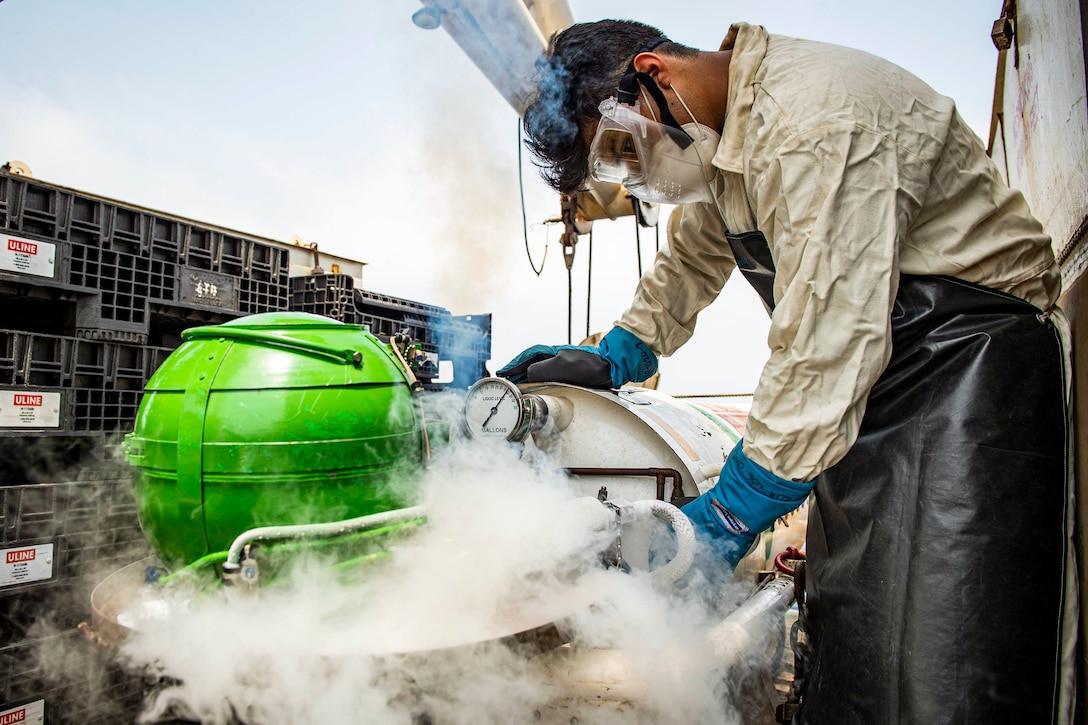 A sailor leans over a green sphere while liquid oxygen smoke rises around it.