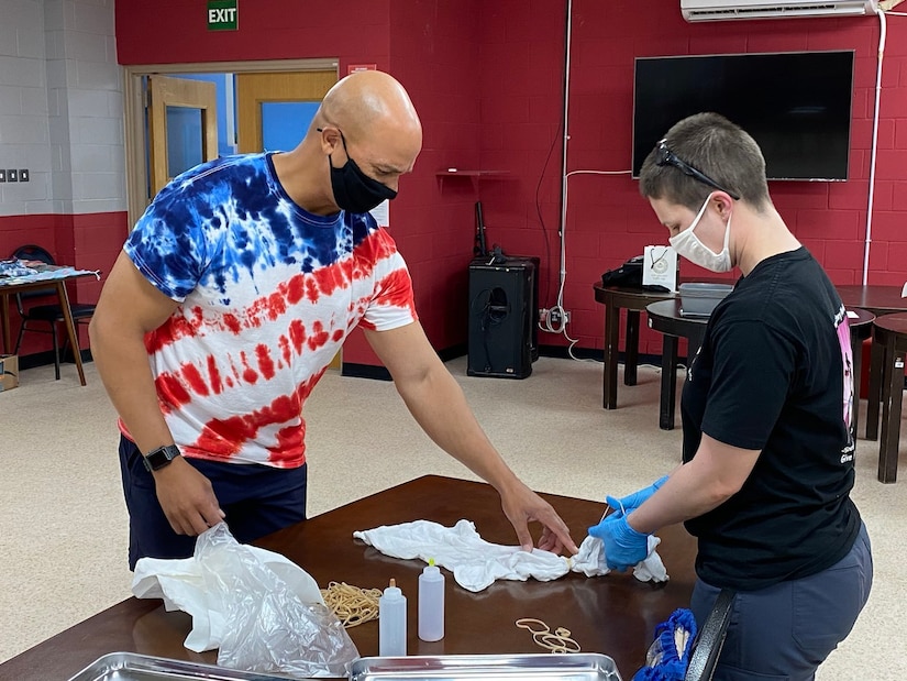 Maj. Anthony Sims-Hall, 1st Theater Sustainment Command, theater mortuary affairs officer, instructs a Soldier on tie-dying techniques at an event held at the MWR building on Camp Arifjan, Kuwait.  Maj. Sims-Hall takes personal passion and hobbies and turns them into resiliency opportunities for Soldiers while deployed.