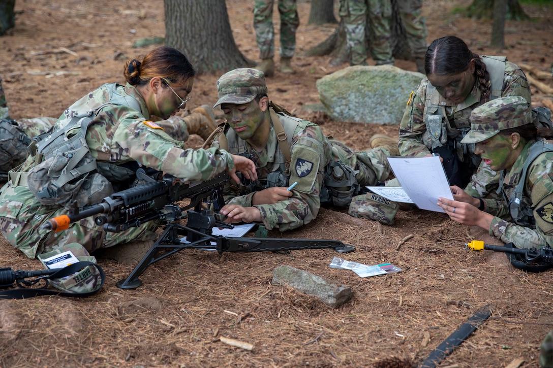A group of soldiers lie together on the ground looking at papers.