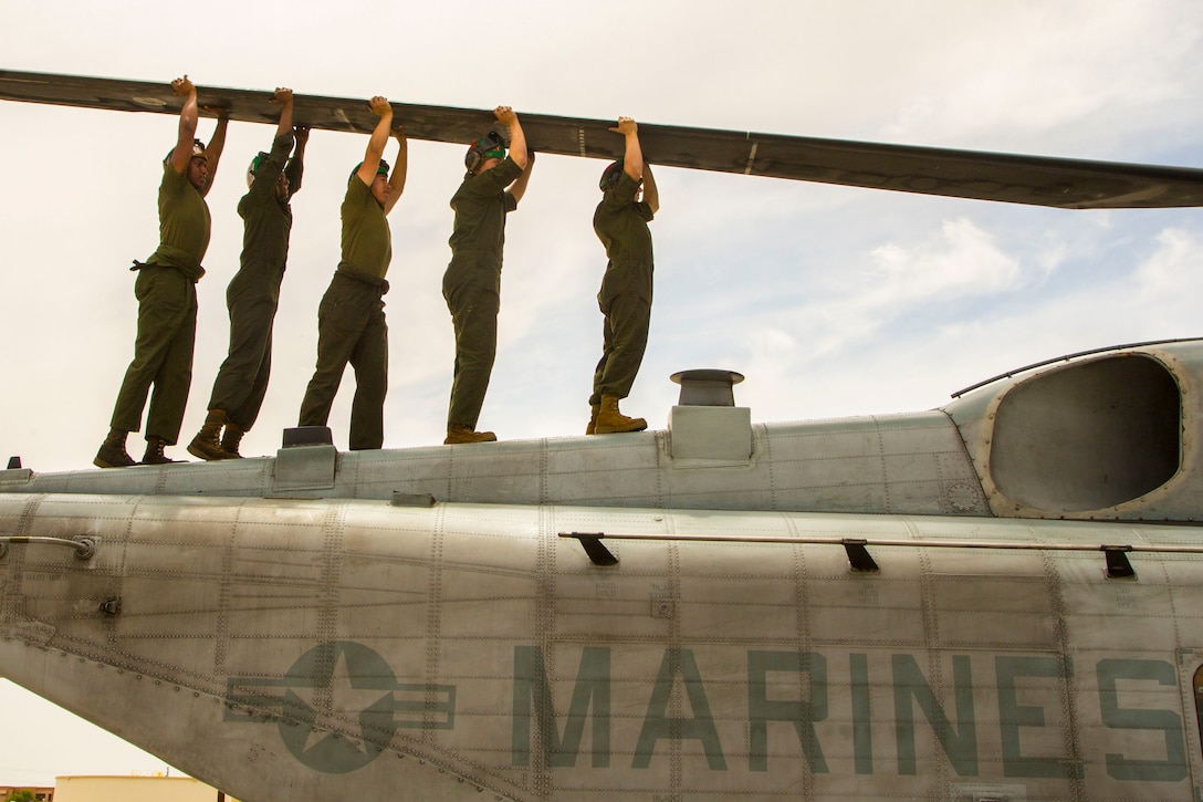 Five Marines carry a large piece of equipment while walking on top of an aircraft.