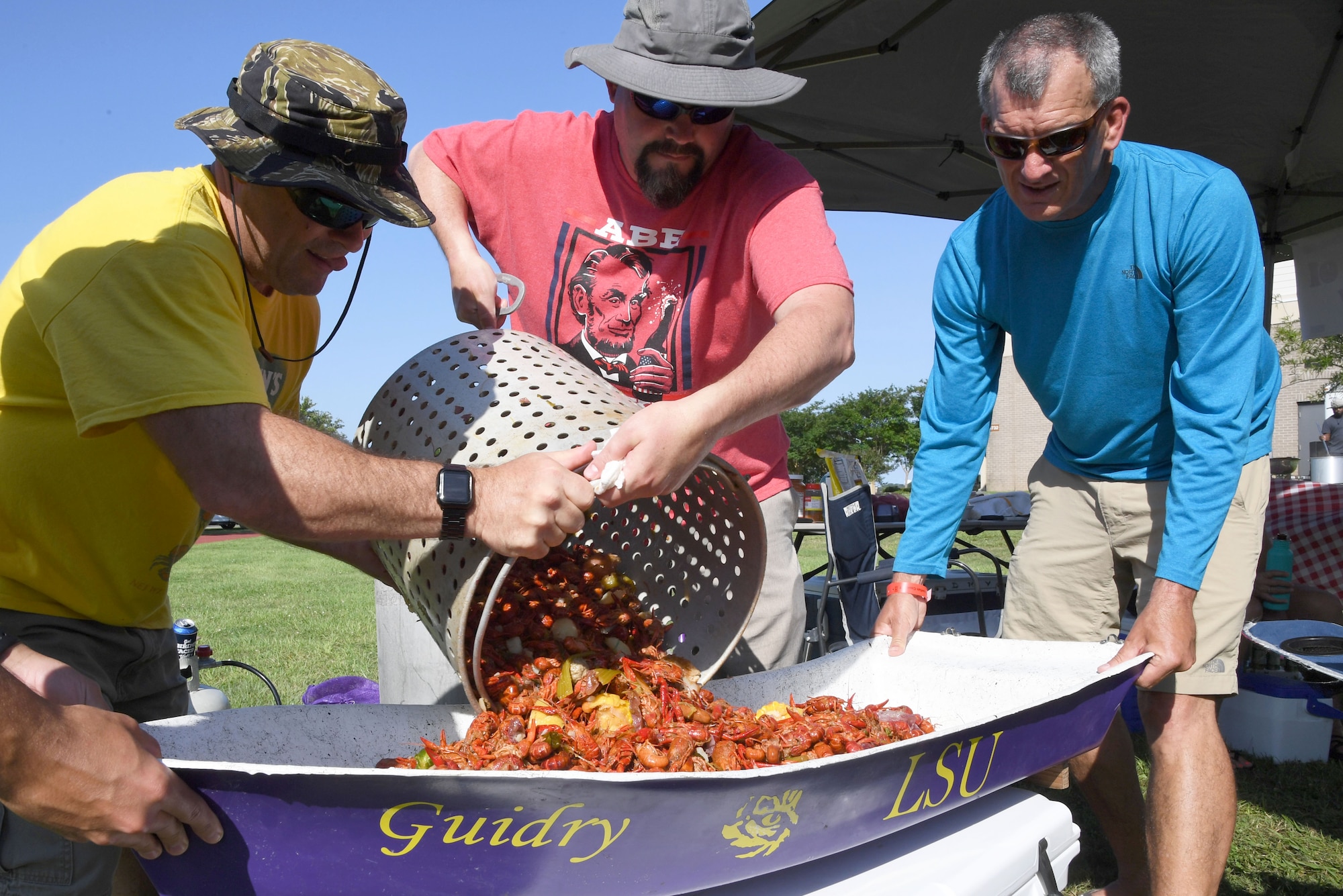 Gary Guidry, Second Air Force curriculum developer, James Reeves, Second AF training requirements action officer, and Joe Taranto, Second AF A3/6 deputy director, pours out a pot of boiled crawfish during the 9th Annual Crawfish Cook-Off at the Bay Breeze Event Center at Keesler Air Force Base, Mississippi, June 11, 2021. Twelve teams competed in the event and more than 800 pounds of crawfish were distributed. (U.S. Air Force photo by Kemberly Groue)