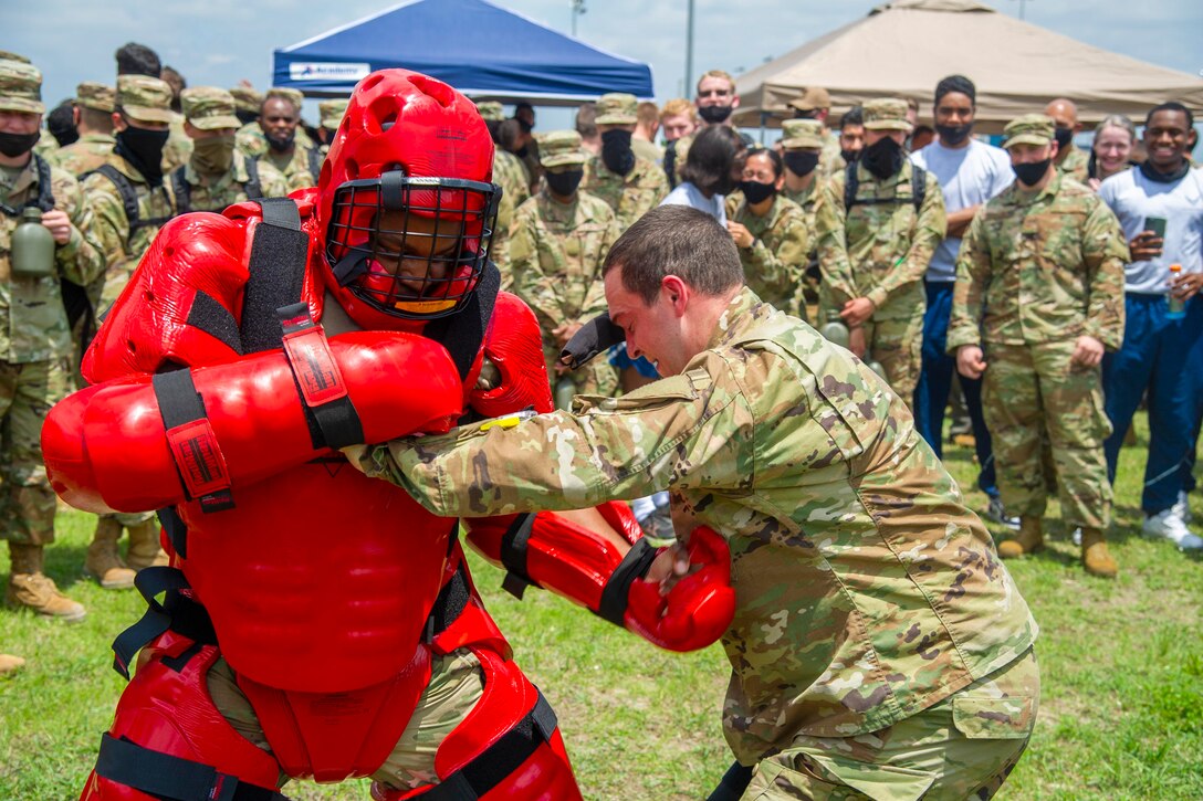 An airman wearing protective gear blocks a punch from another airman.