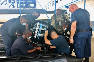 Coast Guardsmen from the U.S., Guyana and Jamaica secure a motor to an inflatable small boat.