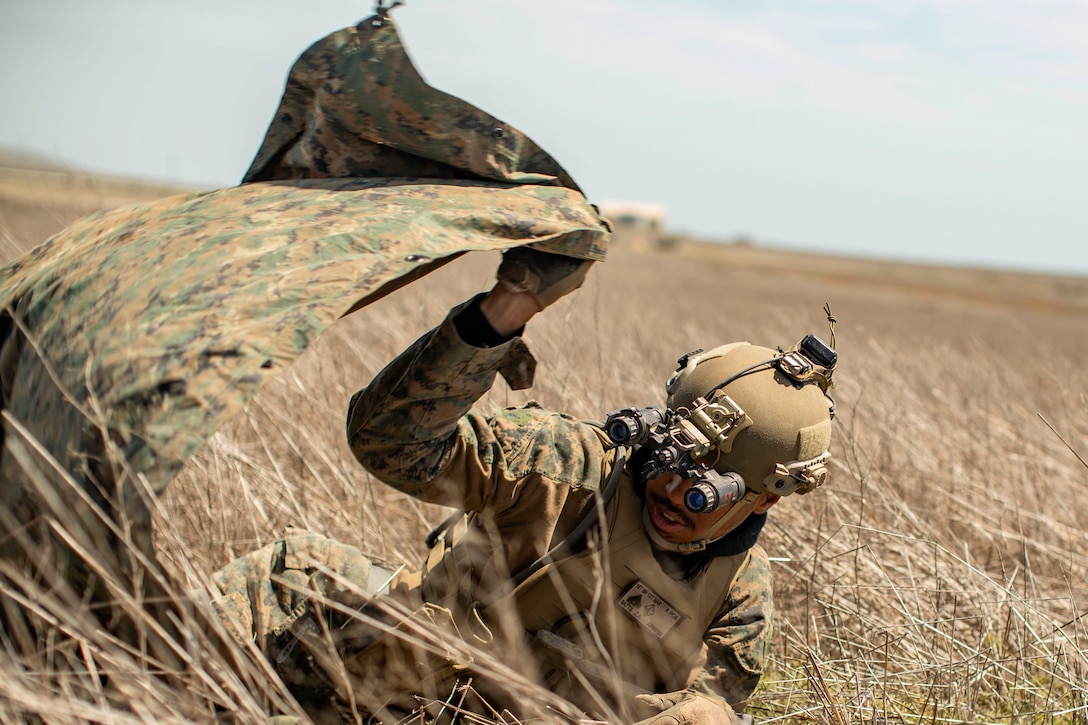 A Marine set up a camouflage tarp in a field.
