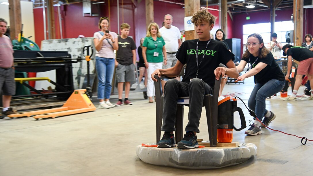 Katy Porter pushes Woody Call on a hoverboard built by LEGACY program students during an open house event in Clearfield, Utah, June 11, 2021. The Leadership Experience Growing Apprenticeships Commited to Youth, or LECAGY program, provides a STEM pipeline that starts with students at age 11 and keeps them in the program until college graduation. (U.S. Air Force photo by R. Nial Bradshaw)