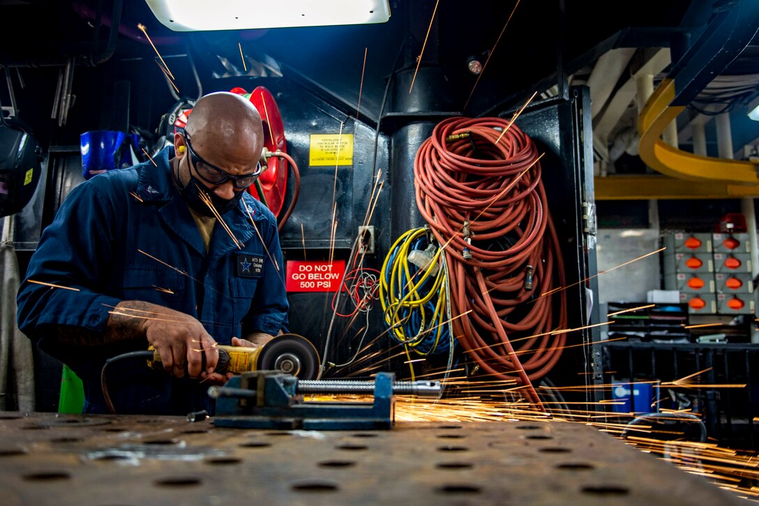 A sailor works with a tool in a shop, creating sparks.