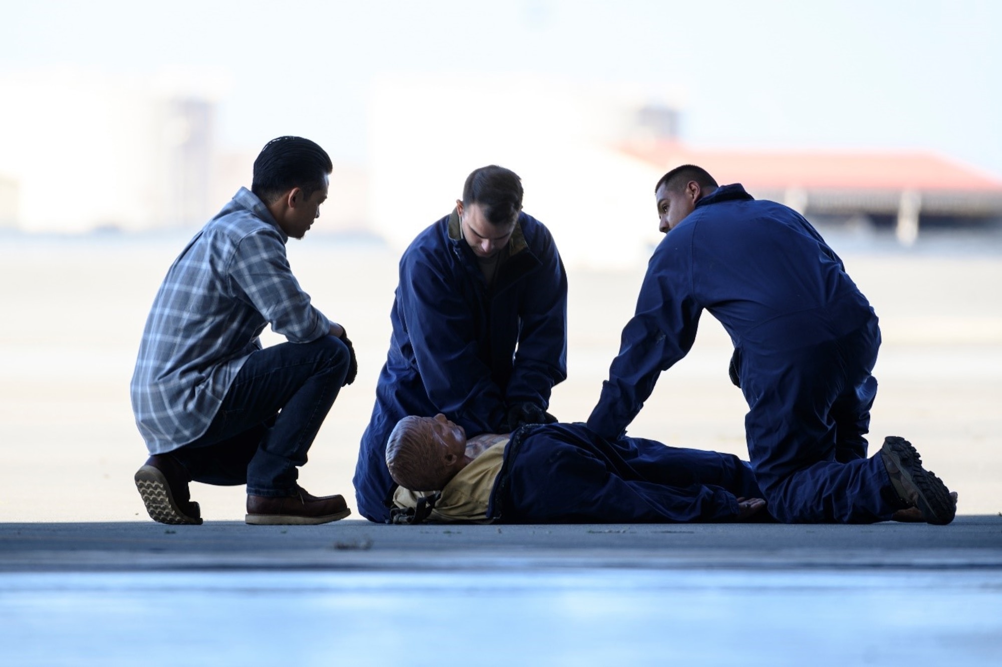 A group of Airmen huddle around a training dummy. The flight line is in the background.