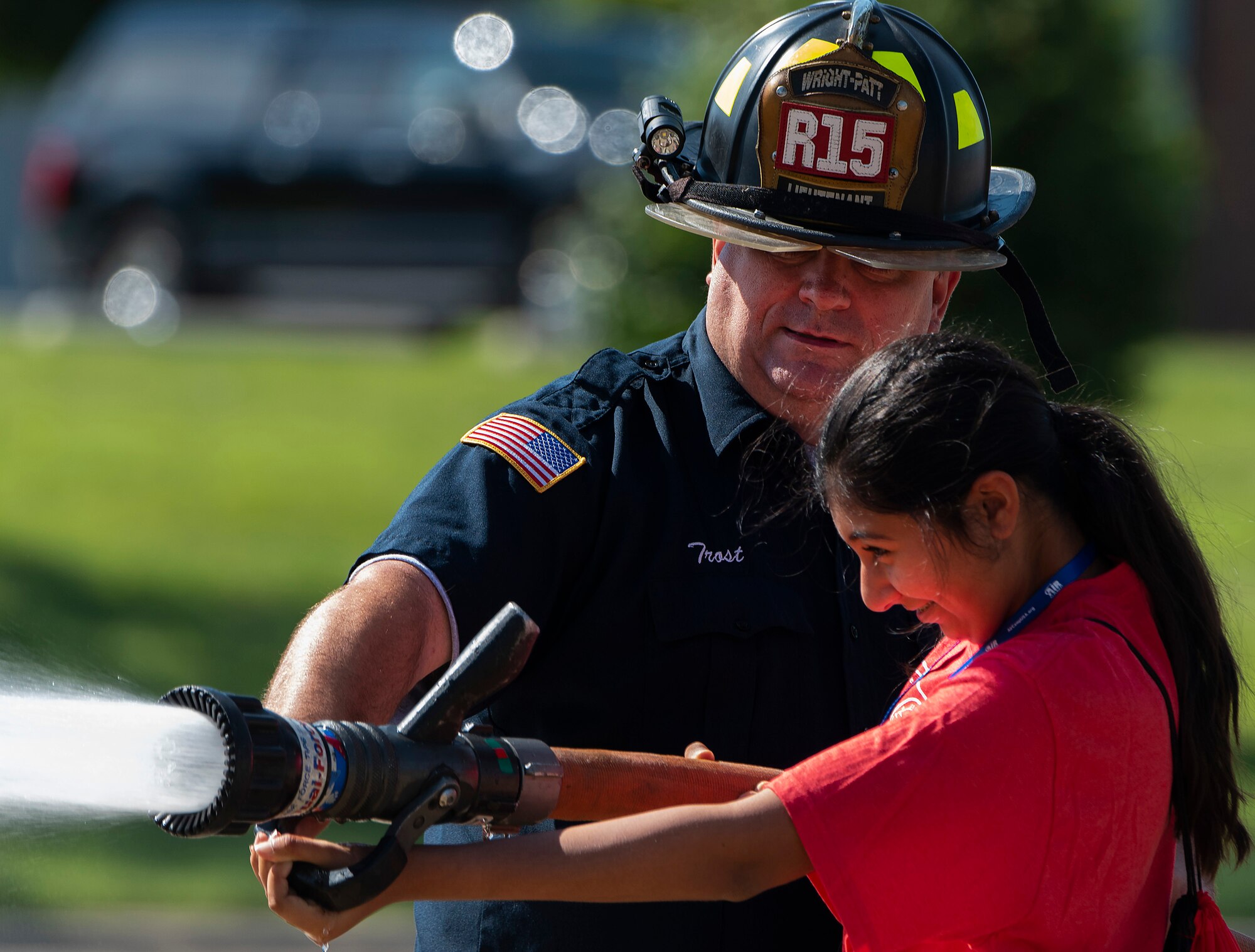 A camper handles a fire hose with the help of firefighter Thomas Trost, 788th Civil Engineer Squadron, at the main fire station on Wright-Patterson Air Force Base, Ohio, June 15, 2021. Air Camp participants came to Wright-Patt to tour aircraft, learn about firefighting and visit the U.S. Air Force School of Aerospace Medicine. (U.S. Air Force photo by R.J. Oriez)